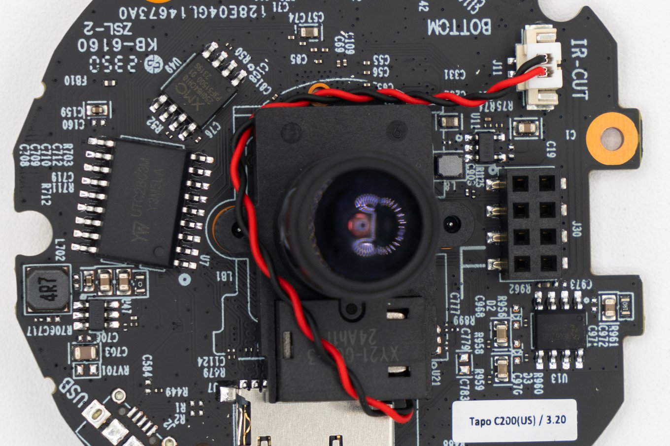 A Tapo C200 security camera’s circuit board: the lens in the centre, an 8-pin SPI flash chip at the upper left